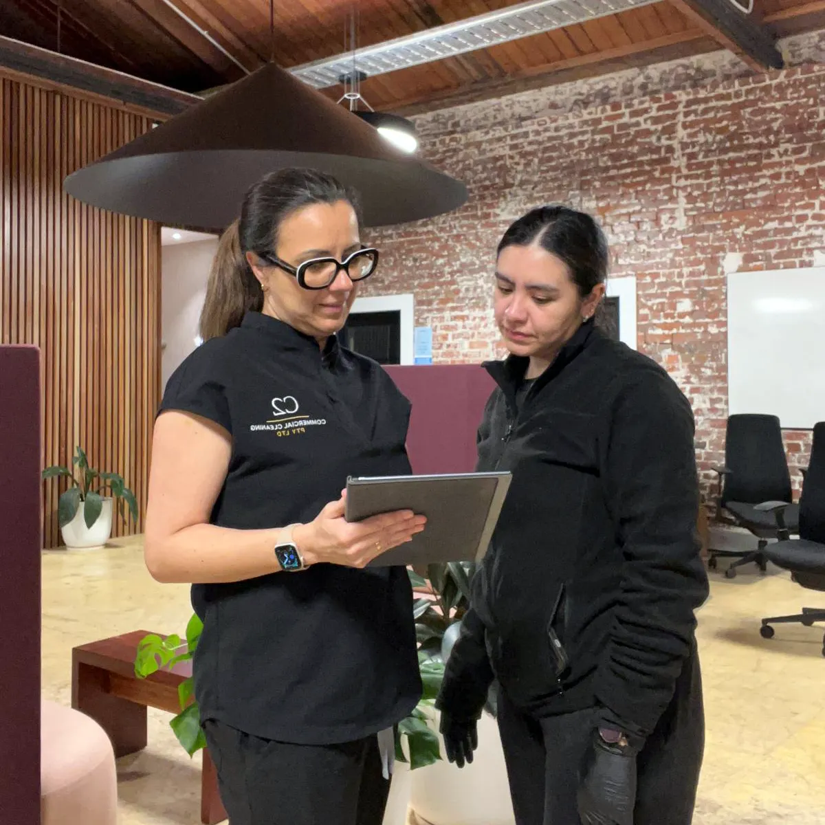 Commercial cleaning representative discussing service details with a workplace manager while a team member cleans nearby